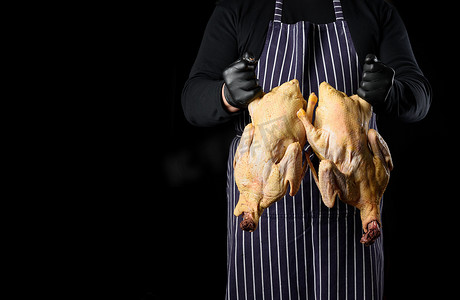 穿着蓝色条纹围裙和黑色衣服的男厨师站在黑色背景上，手里拿着一只鸭子