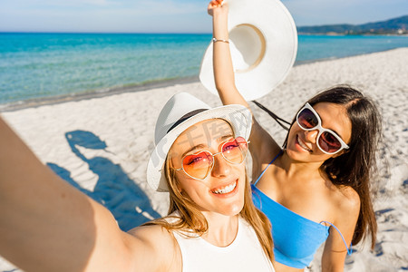 两个戴着白帽子的漂亮女孩在热带海滩度假胜地自拍享受暑假。