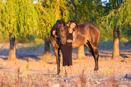 一个骑马的女孩站在树的背景下，落日的光芒落在她们身上