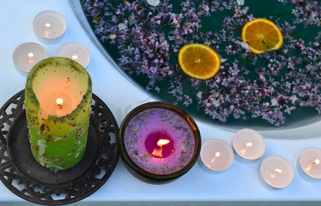 浴缸边上的彩色蜡烛，满是蓝色的水和紫丁香花