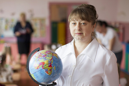 白俄罗斯，戈梅利市，2019 年 5 月 10 日。幼儿园开放日。一位带地球仪的老师的肖像。老年女教师。