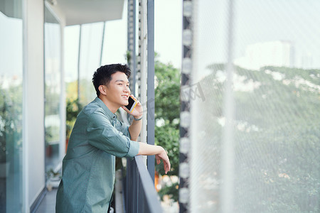 笑着打电话摄影照片_亚洲男人用智能手机聊天，笑着大笑，在阳台上放松