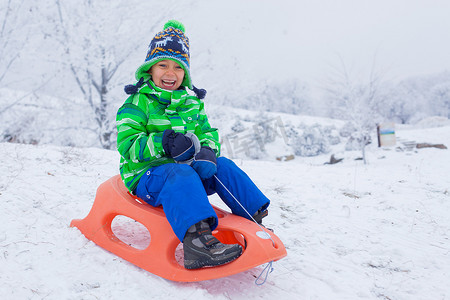 在冬季公园玩雪橇的小男孩