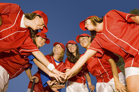快乐的女垒球运动员双手叠放在清澈的蓝天上