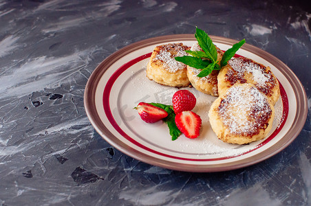 美食早餐-凝乳煎饼、芝士蛋糕、凝乳煎饼、草莓、薄荷和糖粉放在白盘子里。