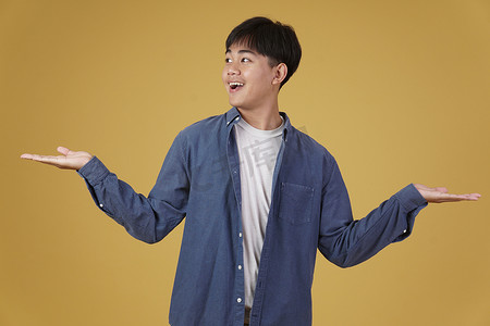 兴奋、快乐、英俊的亚洲年轻男子的肖像，穿着随意，微笑着，在黄色背景中张开手势