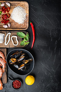 黑色混凝土表面带虾和墨鱼的西班牙海鲜海鲜饭配料，平铺，带复制空间