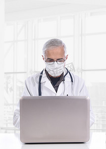 在现代医疗设施中，戴着外科口罩的中年医生坐在办公桌前使用电脑。