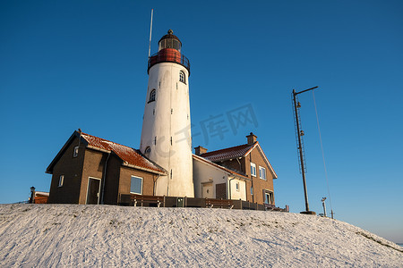 urk摄影照片_Urk 的冬天，Urk 灯塔旁的堤坝和海滩在冬天被雪覆盖，Urk Flevoland 灯塔旁的日落