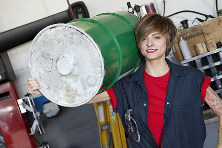汽车车间肩扛油桶的快乐年轻女机械师画像