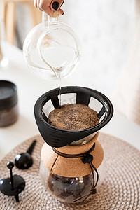 年轻女子在 chemex 中冲泡咖啡，将热水倒入过滤器