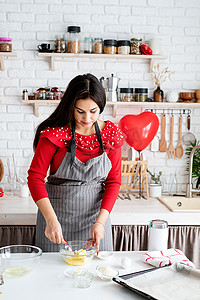 穿着红色连衣裙和灰色围裙的女人在厨房做情人节饼干