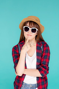 思考方式摄影照片_美丽的肖像年轻亚洲女性戴着太阳镜和帽子，背包微笑自信地享受暑假孤立的蓝色背景，旅游模特女孩思考想法规划旅游概念。