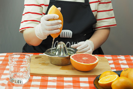 一名年轻女子在手工榨汁机上用橙子和葡萄柚鲜榨果汁。