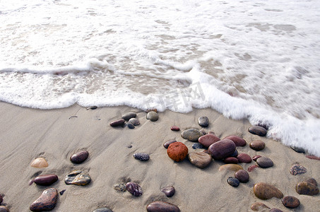 海边躺摄影照片_海浪拍打着躺在海岸线上沙子里的石头。