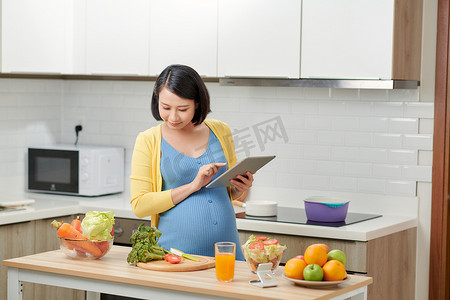 孕妇在餐桌上的食物附近使用数字平板电脑