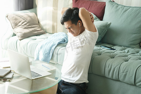亚洲年轻学生男子企业家戴着耳机，在家里用电脑学习在线学习时，会感到疲倦、无聊、困倦。