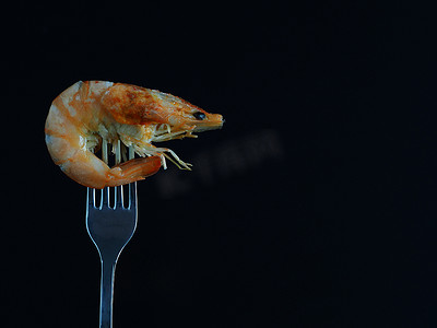 虾在黑色背景上孤立地放在叉子上，没有去皮。