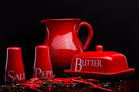 深色光晕背景摄影照片_Cristina Arpentina 设计的深色背景中的红盐瓶、胡椒盒、黄油和水罐