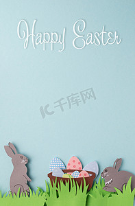 兔兔图案摄影照片_复活节快乐手工贺卡与纸兔、装饰鸡蛋和绿草。