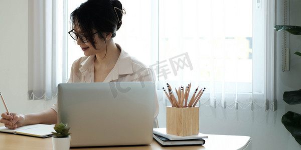 女性在办公桌前做笔记，同时在线学习，在笔记本电脑听力学习课程会议上观看网络研讨会播客，电子学习概念