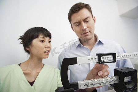 头部摄影照片_医院护士旁边站在体重秤上的男人