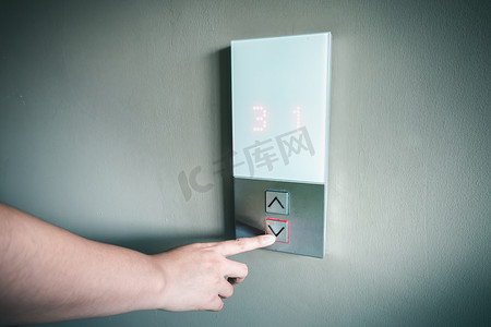 女人手的特写是按下电梯按钮进入办公楼，电动电梯按钮控制在建筑物内上下移动楼层。