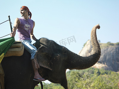 年轻人骑大象侧视，从背景中的肩山望去