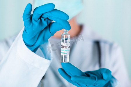 身穿制服和戴面罩的手套的医生或护士在实验室拿着带有 COVID-19 冠状病毒疫苗标签的药瓶疫苗瓶