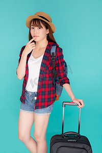 美丽的年轻亚洲女人拉着蓝色背景中突显的手提箱，有表情的亚洲女孩带着兴奋、旅行和旅行的概念快乐地拿着行李在假期中行走。