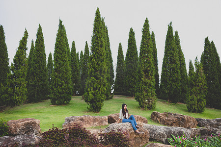 草坪和人摄影照片_独自坐在石头和松树上的女人