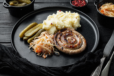 烧烤配菜摄影照片_Wurst 或 Bratwurst，配发酵卷心菜、腌黄瓜和香料，黑色木桌背景