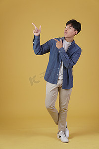快乐英俊的亚洲年轻男子的肖像，穿着随意，手指指向黄色背景中孤立的复制空间