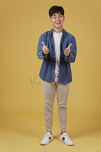 盖中盖表情摄影照片_面带微笑、积极向上的亚洲年轻男子的肖像，穿着随意，大拇指竖起，赞同黄色背景中孤立的表情