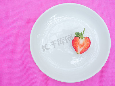 单红心草莓甜果红色浆果心形水果的特写质地，在粉红色织物背景的白盘中切成两半