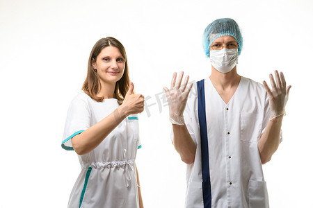一名护士站在一名戴着医用口罩、帽子和无菌手套的医生旁边，高兴地向上指着