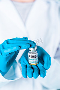 大药瓶摄影照片_女医生或护士穿着制服和戴面罩的手套在实验室拿着带有 COVID-19 冠状病毒疫苗标签的药瓶疫苗瓶
