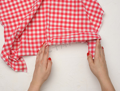 两只女手拿着白桌上皱巴巴的白红方格纺织厨房餐巾