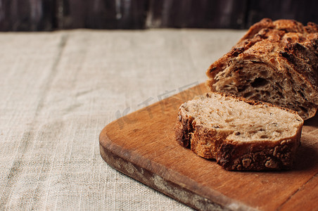 切好的无酵母黑荞麦面包放在木桌上的木板上，木桌上铺着乡村风格的亚麻桌布。