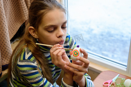 女孩坐在靠窗的桌子旁画复活节彩蛋