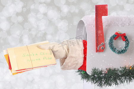 圣诞老人的手臂拿着一堆圣诞信件，这些信件从带有银色散景背景和雪花效果的邮箱里出来。
