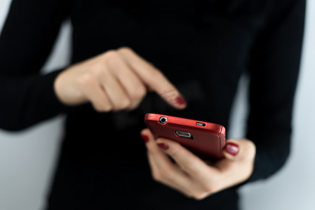 年轻女性手持带摄像头的红色手机的特写细节，使用带有应用程序的触摸屏连接社交媒体、短信、聊天和消息