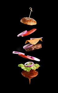 神采飞扬摄影照片_经典芝士汉堡芝麻面包、洋葱圈、番茄片和多汁烤肉排的飞扬成分