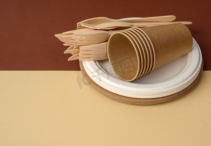 纸杯和木叉，棕色背景上用回收材料制成的空圆形棕色一次性盘子