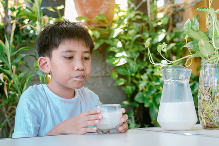 奶渍牛奶摄影照片_男孩喝完杯子里的牛奶后，嘴角沾满了奶渍。