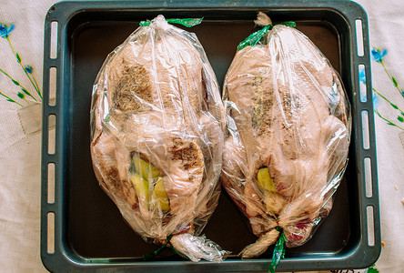 两只新鲜生的整只鸭子放在托盘上，上面放着烘焙用的配料和香料。