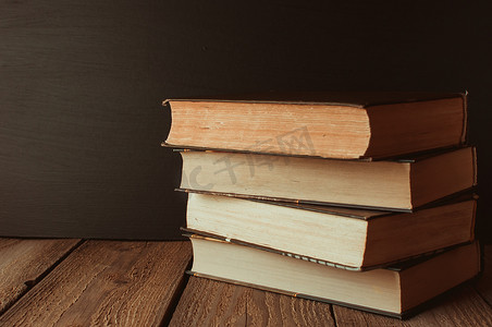 学校黑板背景下以乡村风格堆放在木桌上的书籍。