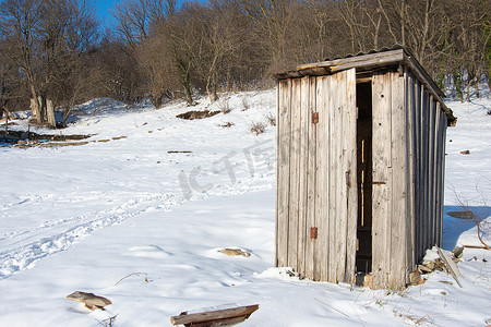 一个古老的木制街道厕所独自矗立在一片空旷的积雪地块上