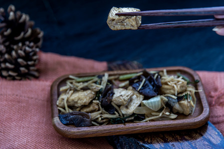 炒豆腐摄影照片_手正用筷子夹起木盘里的姜炒豆腐。