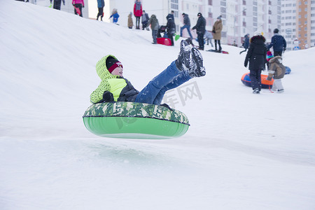 玩1摄影照片_白俄罗斯，戈梅利市，2018 年 1 月 7 日。中央公园。儿童雪橇芝士蛋糕。从雪滑梯上拉雪橇。一个男孩在雪橇管上从跳板上跳下。
